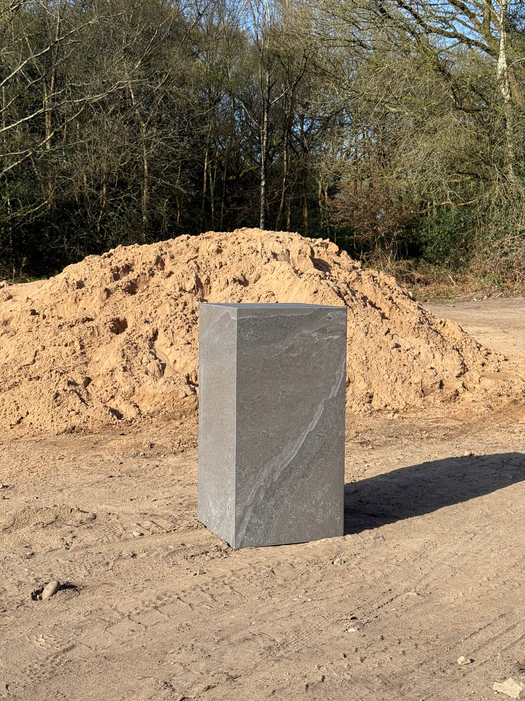 Dark grey matte porcelain side table photographed outdoors, showing full form and scale